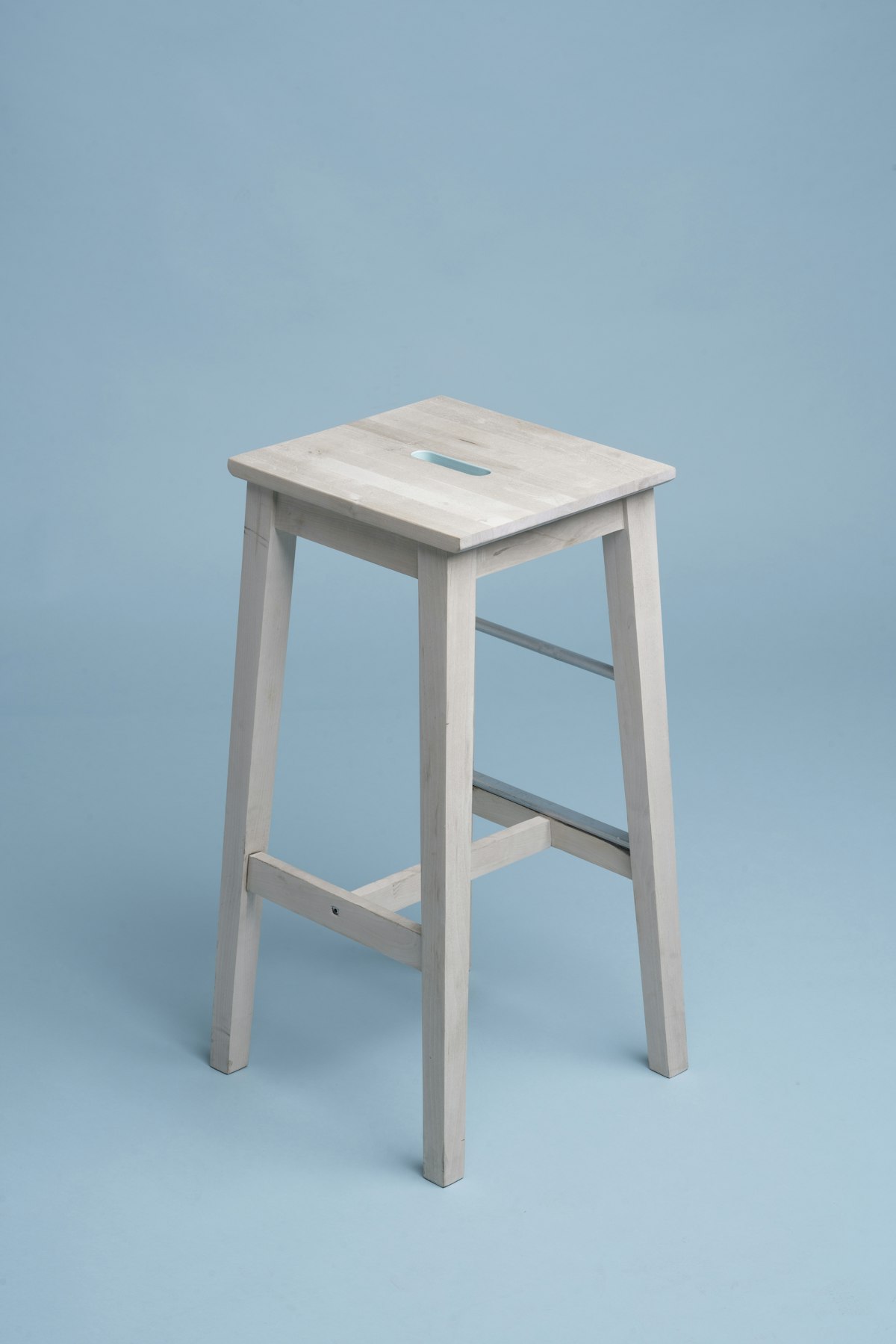 Pale wooden bar stool with a hand-hold cut into the seat