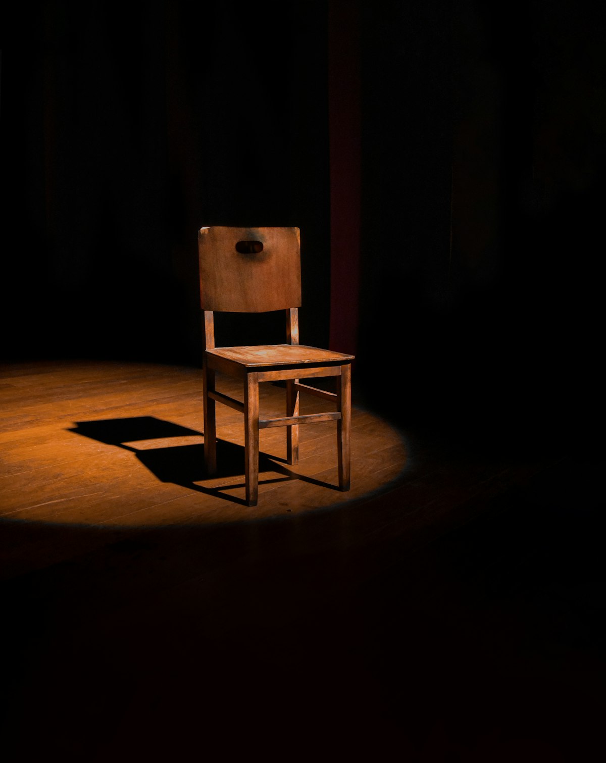 Simple wooden side chair lit by a single overhead spotlight